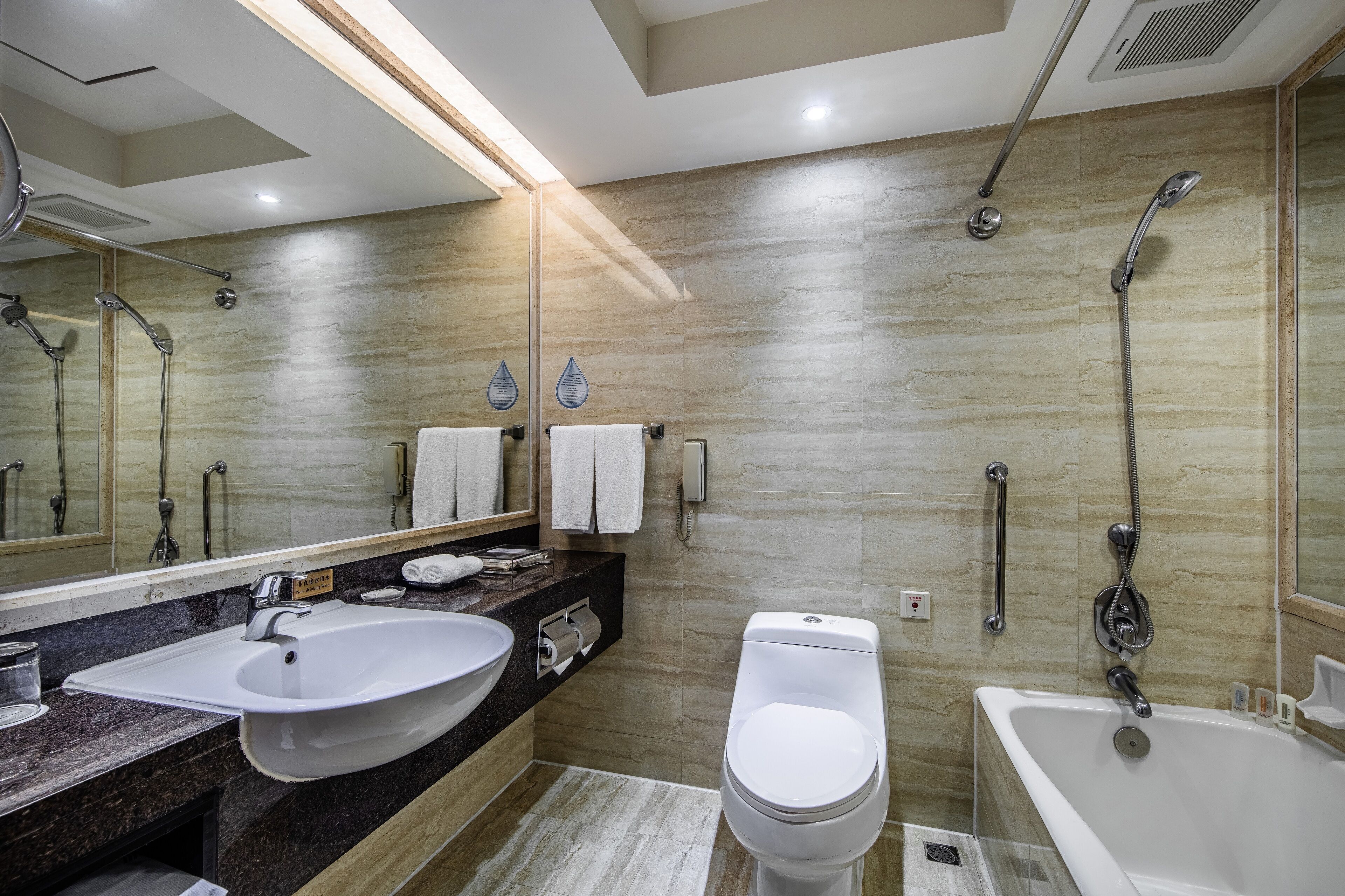 A modern bathroom with a sink, toilet, and bathtub, featuring a marble wall and a large mirror.