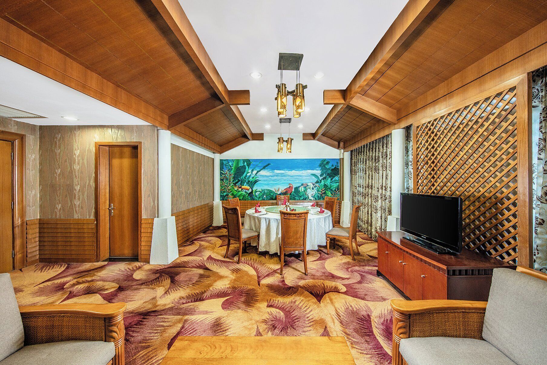 A room with a round dining table, wooden chairs, a television, and a patterned carpet.