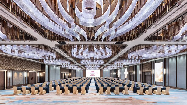 A large conference room with rows of tables and chairs, a central stage, and a modern chandelier. - Crowne Plaza Foshan by IHG (Foshan)