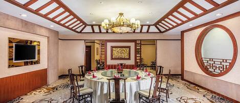 Un comedor de hotel con una mesa redonda, sillas, una araña, un televisor y un espejo grande.