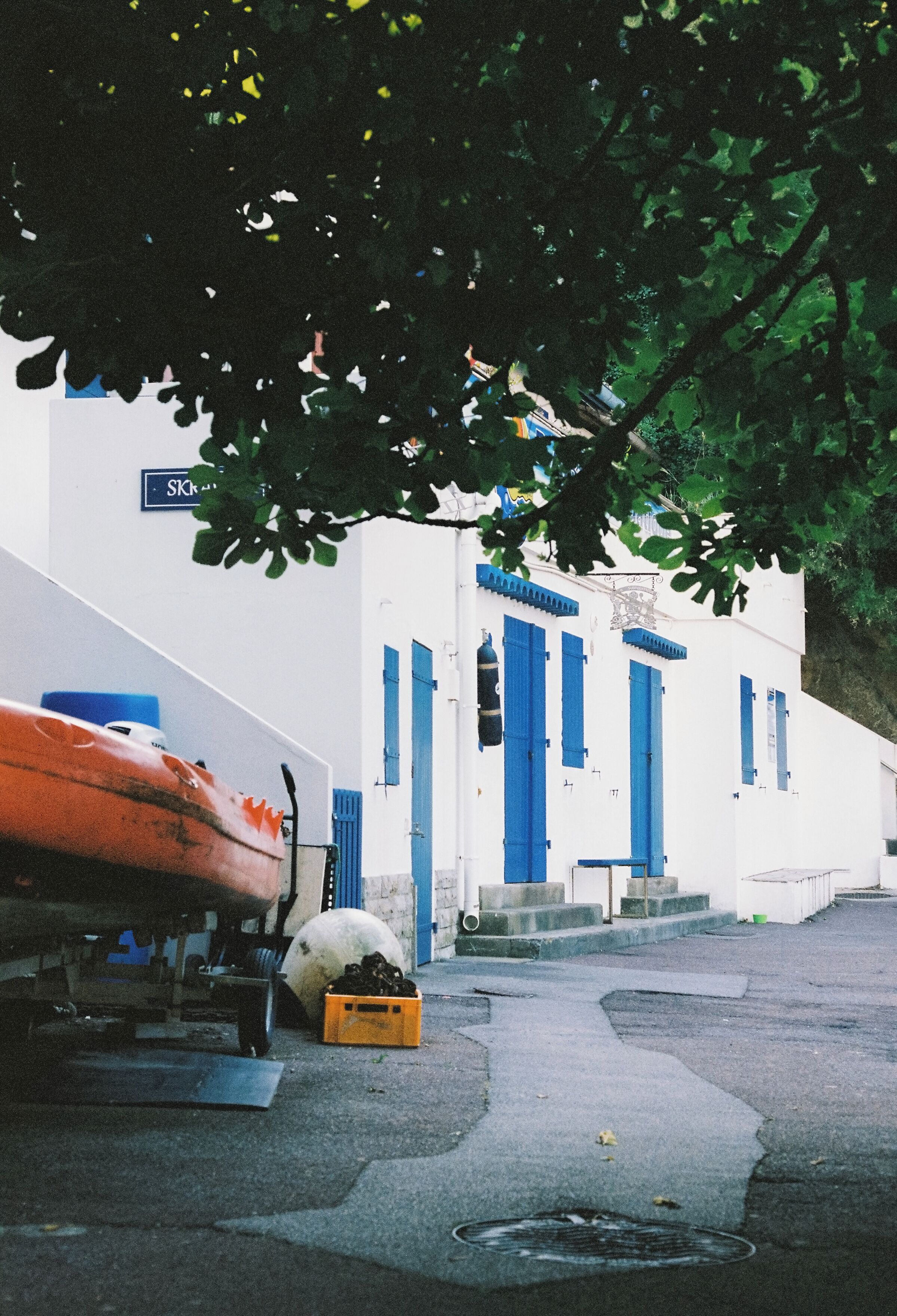 A white building with blue doors and windows, a boat, and a yellow crate on the ground.