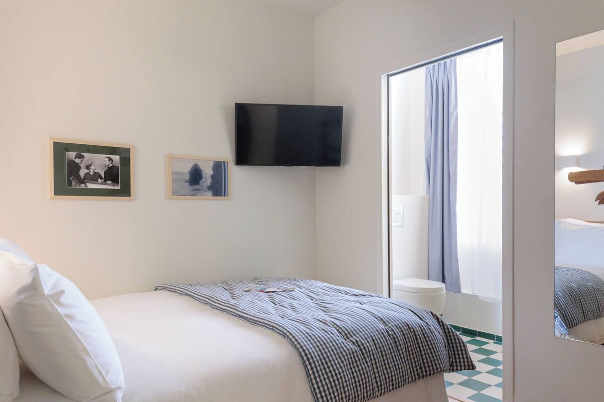 A bedroom with a bed, a television mounted on the wall, and a window with curtains.
