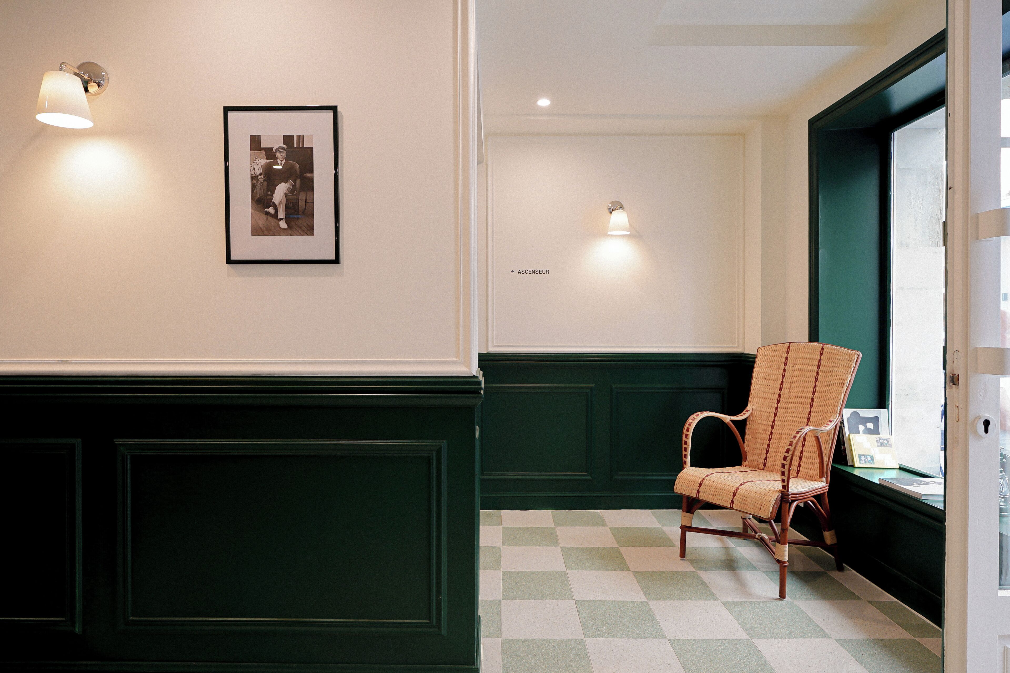 Una habitación con piso a cuadros, una silla de mimbre y dos lámparas fijadas a la pared.