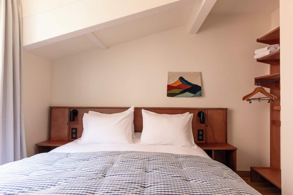 A neatly made bed with a checkered bedspread, a wooden headboard, and a wall-mounted artwork.