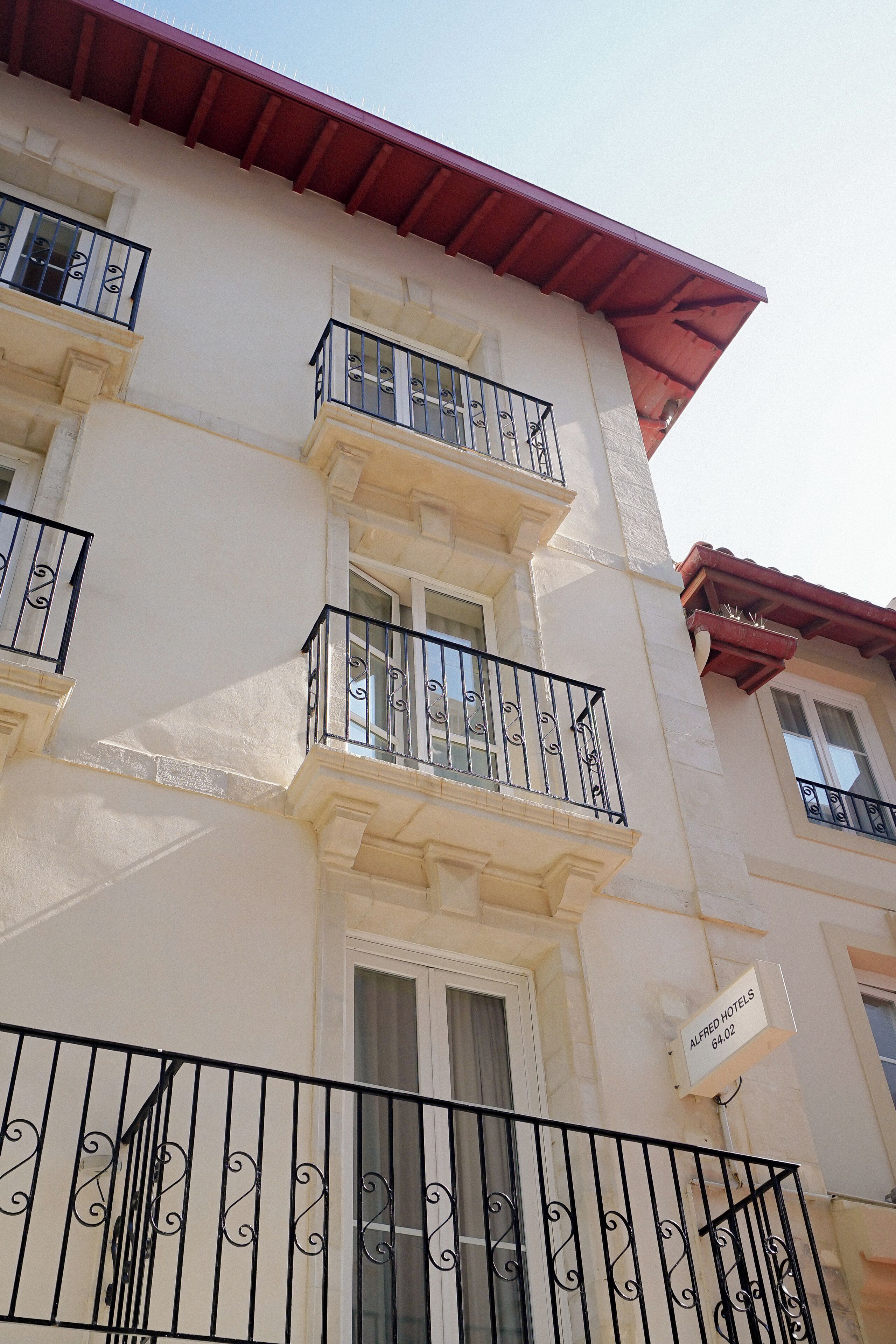 A multi-story building with balconies, a sign indicating 'Alfred Hotels', and a red roof.
