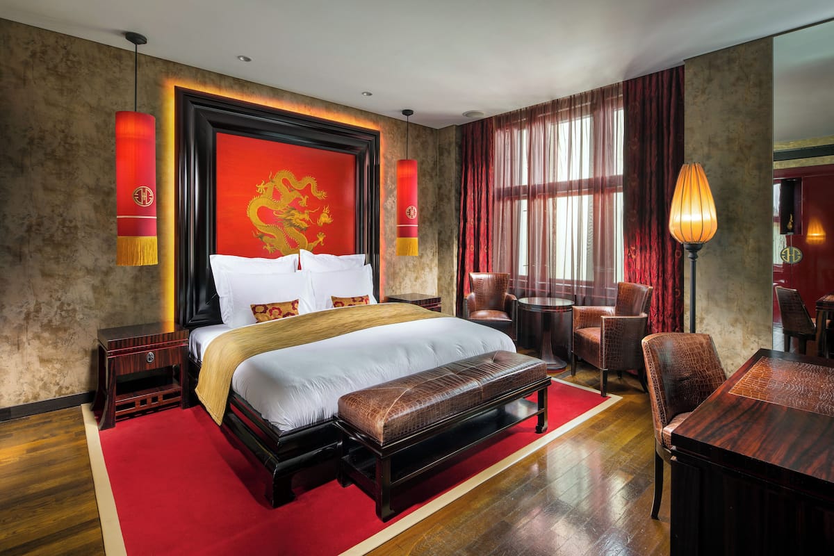 A hotel room with a large bed, a wooden bench, a dining table, and a red carpet.