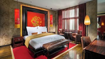 Habitación de hotel con una cama grande, un banco de madera, una mesa de comedor y una alfombra roja.