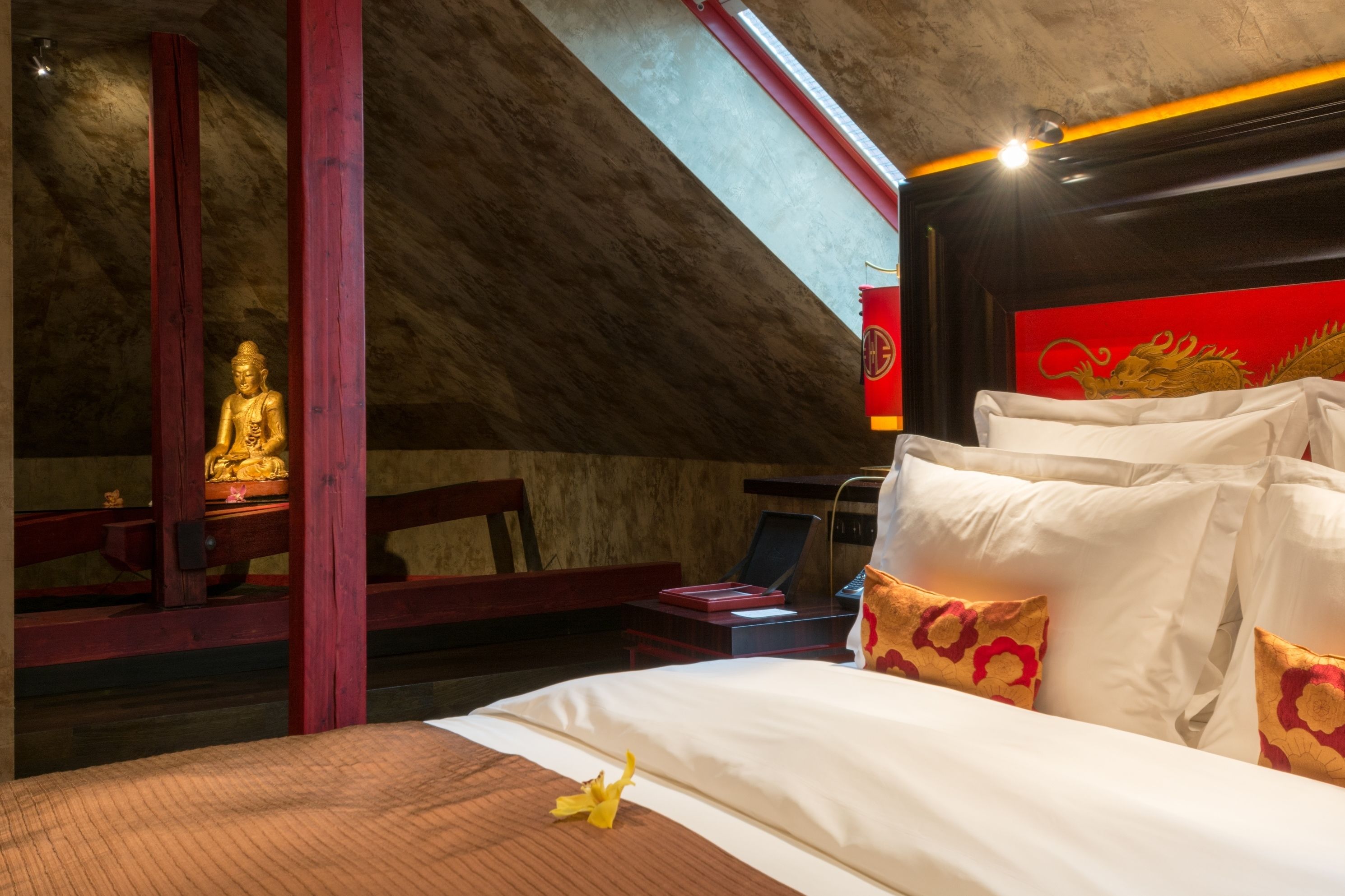 A room with a bed, a statue, and a red wall with a dragon design.