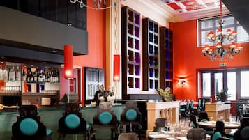 A restaurant with a high ceiling, ornate chandeliers, and a bar area.