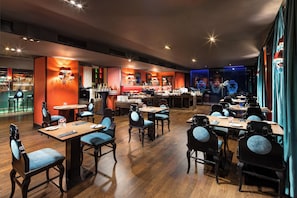 A restaurant with wooden flooring, blue upholstered chairs, and tables.