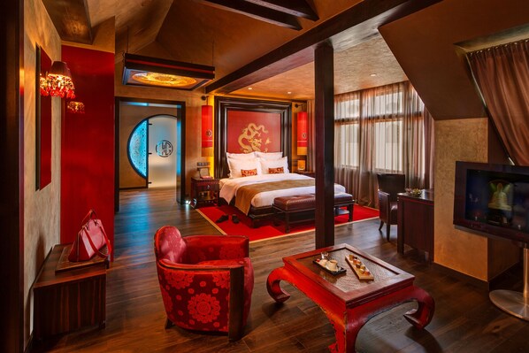 A hotel room with a large bed, a TV, a red armchair, and a wooden coffee table.