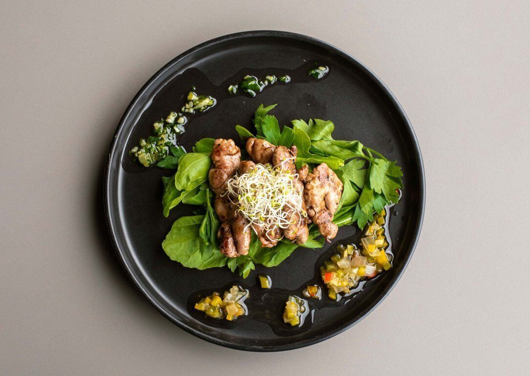 A black plate with grilled chicken, sprouts, and a green salad on a neutral background.