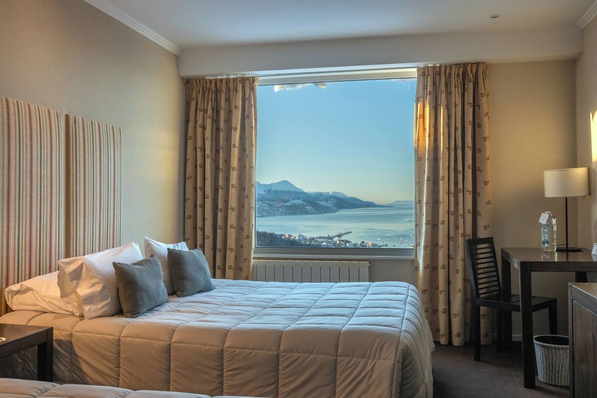 A hotel room with a large bed, a desk, and a view of a coastal landscape.