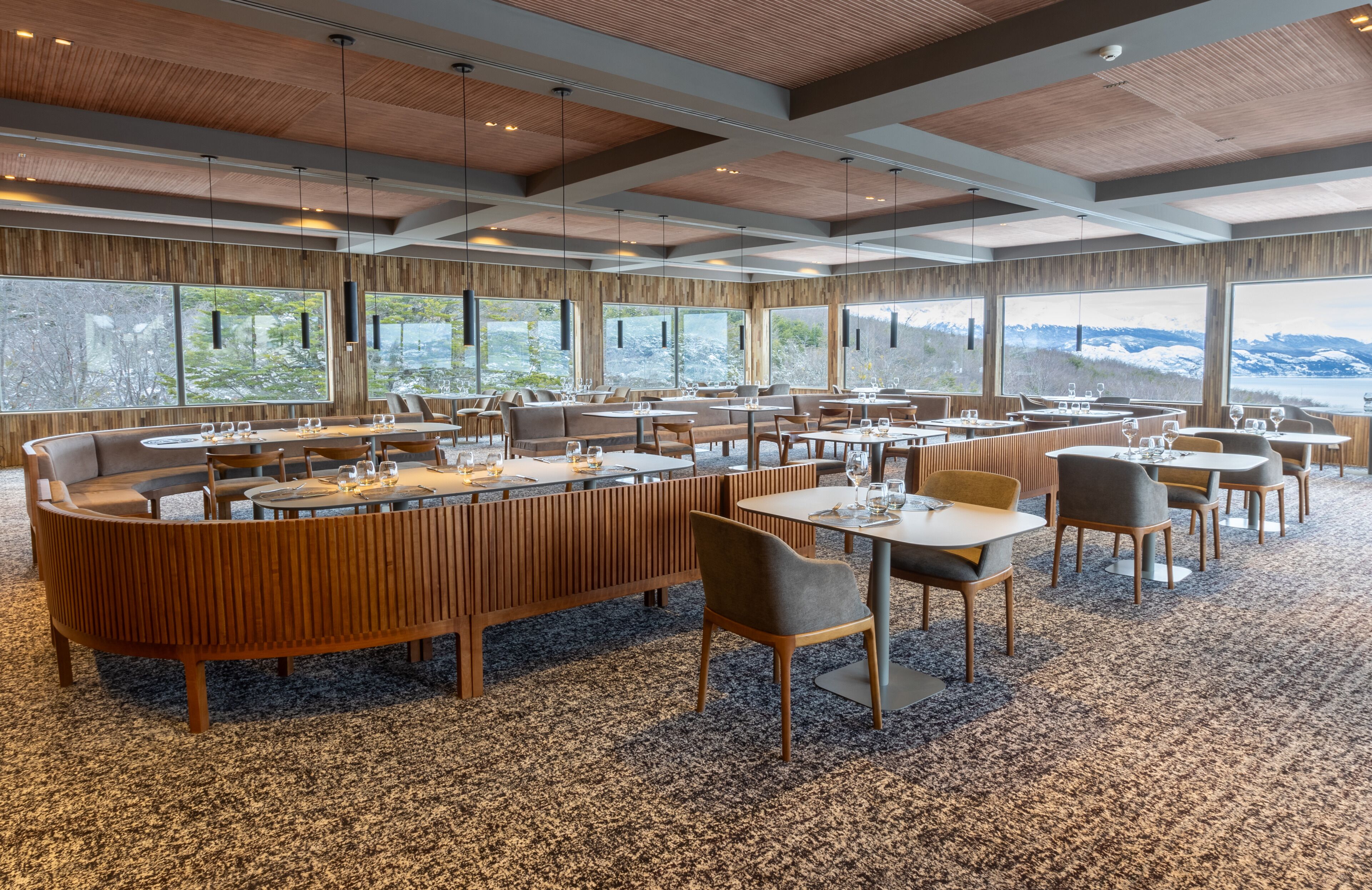 Un'ampia sala ristorante con soffitto alto, ampie finestre che offrono viste panoramiche sulle montagne e diverse tipologie di posti a sedere, tra cui tavoli rotondi e banconi.