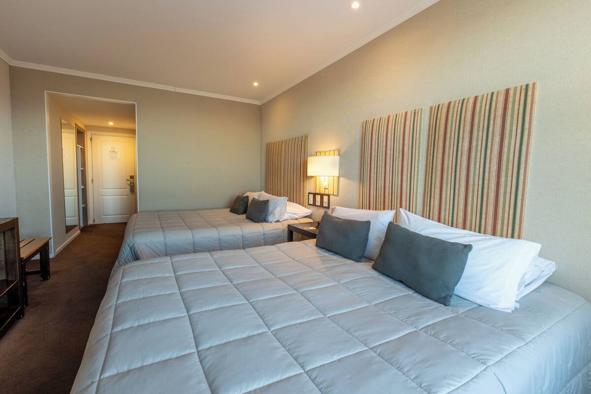 A hotel room with two beds, a bedside table, a lamp, and a striped wall decoration.