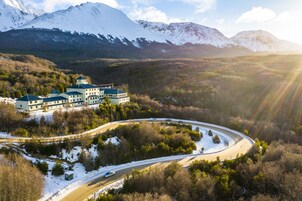 Un edificio grande de varios pisos con un camino curvo, rodeado de colinas y árboles cubiertos de nieve.