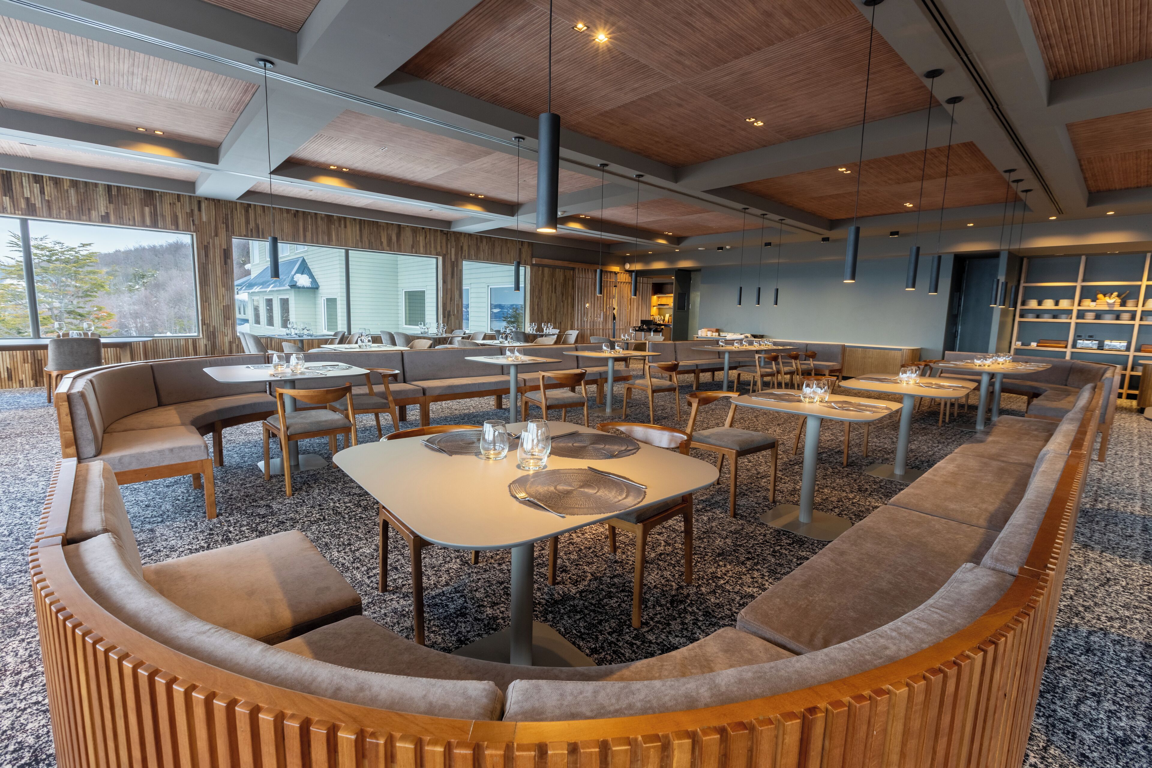 A modern dining area with wooden accents, multiple seating options, and large windows offering views of the outside.