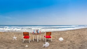 A beach with two wooden chairs and a table with a red cushion, a starfish, and a seashell. - Club Mahindra Puducherry (Bahur)
