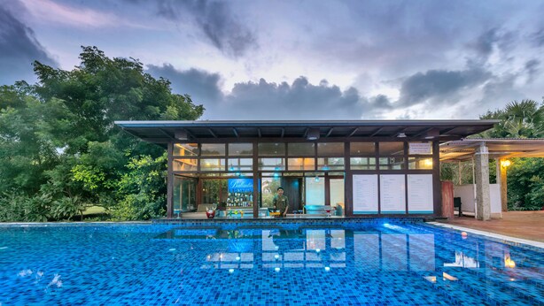 A swimming pool with a tiled deck, a covered seating area, and a bar. - Club Mahindra Puducherry (Bahur)