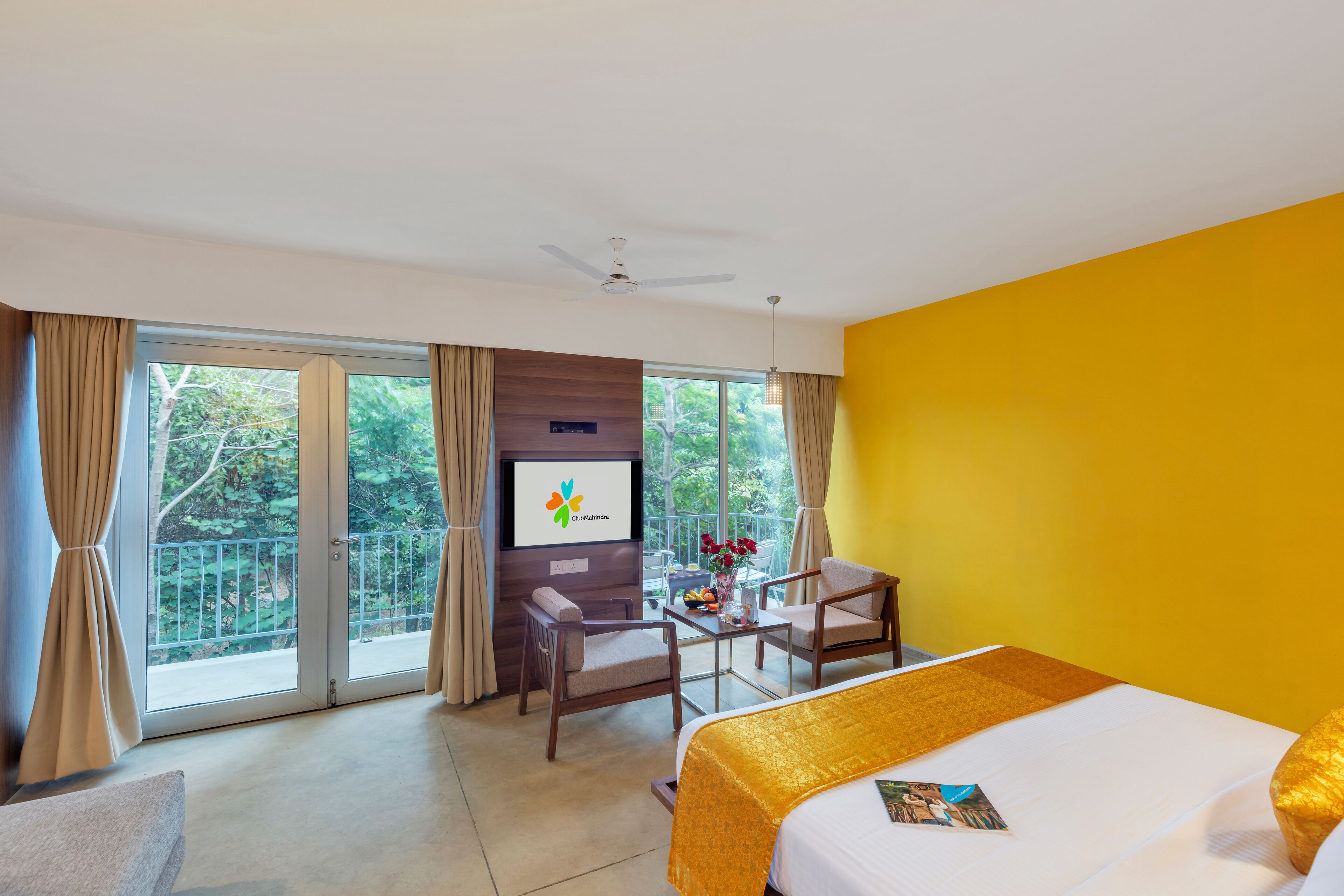 A hotel room with a bed, a desk with a chair, a TV, and a balcony with curtains.