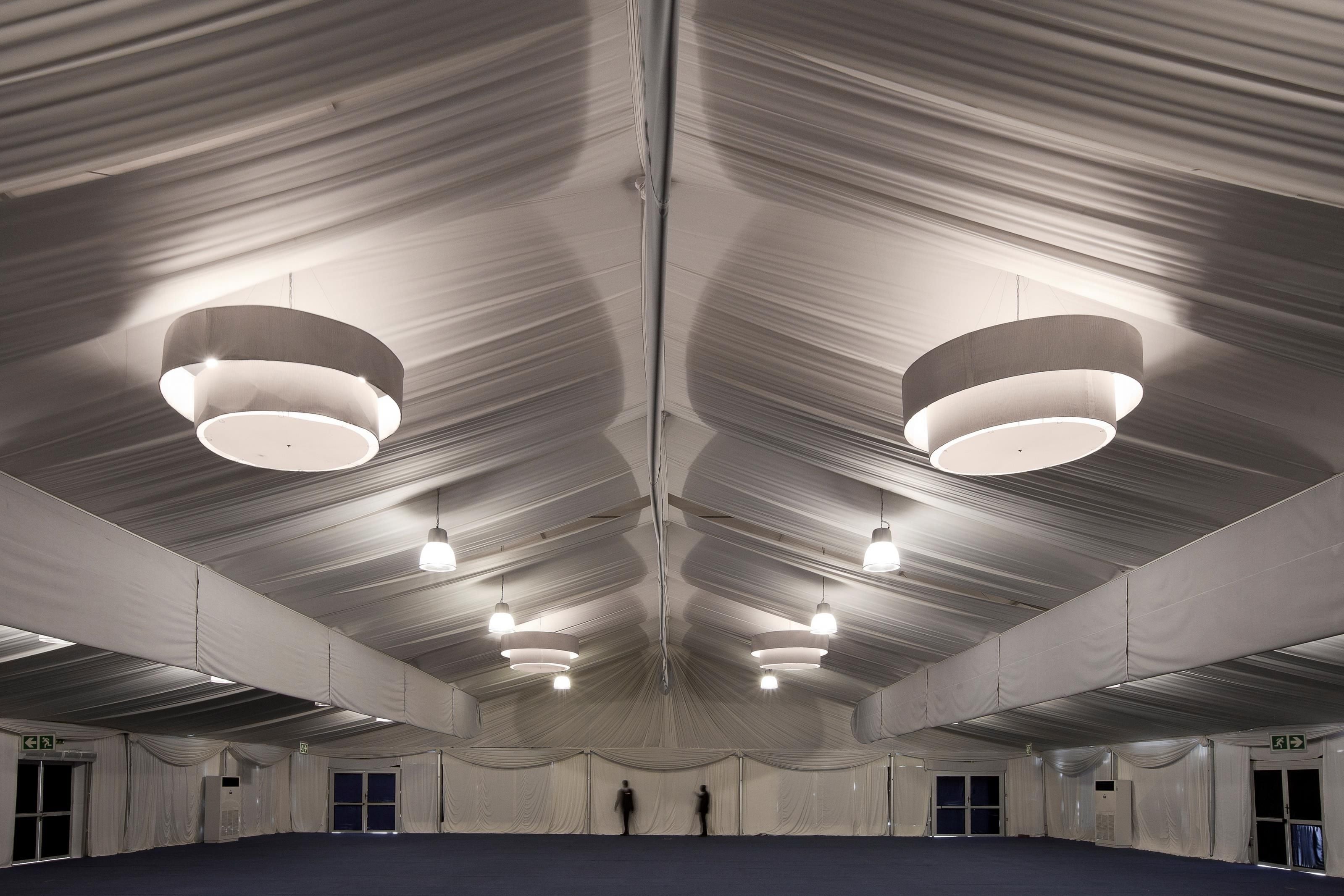 A large indoor space with a high ceiling, multiple hanging lights, and a central aisle.