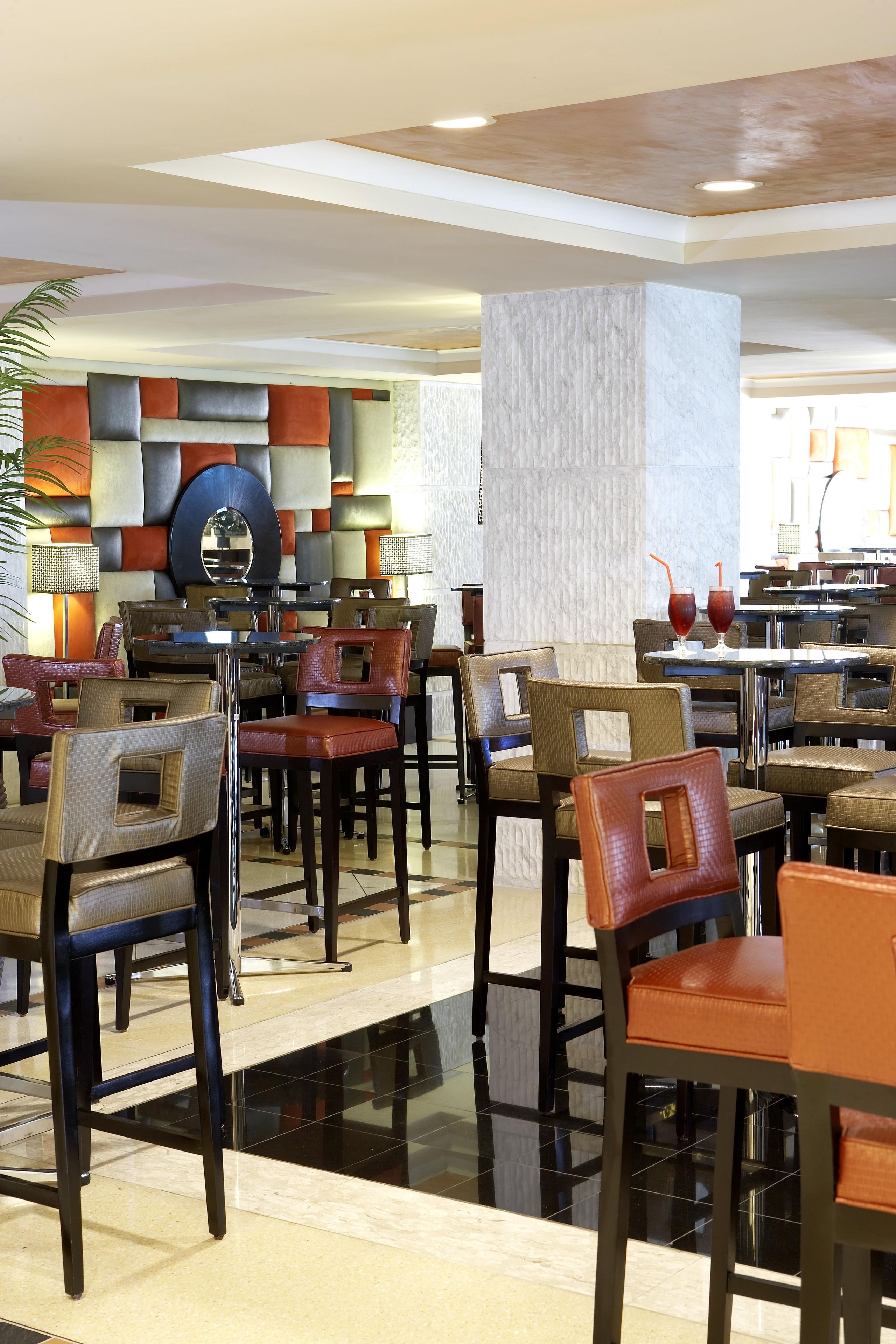 Un vestíbulo de hotel con varias mesas y sillas de comedor, un espejo grande y una pared decorativa.