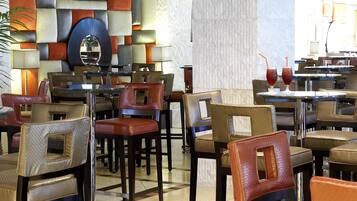 Un vestíbulo de hotel con varias mesas y sillas de comedor, un espejo grande y una pared decorativa.