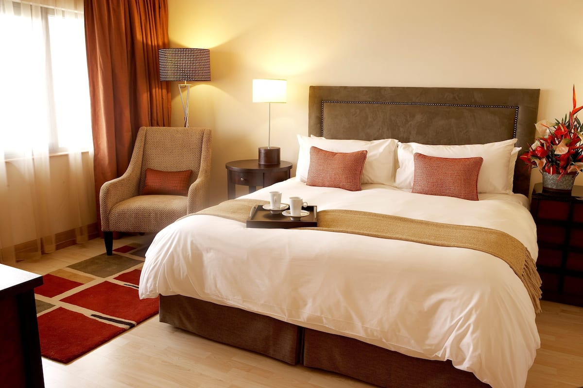 A hotel room with a large bed, a chair, a nightstand, and a lamp.