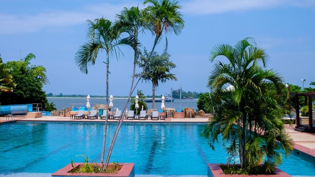 A swimming pool with lounge chairs and palm trees, overlooking a body of water.