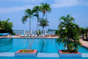 A swimming pool with lounge chairs and palm trees, overlooking a body of water.