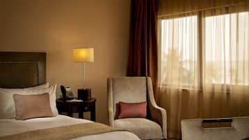 Une chambre d’hôtel avec un lit, une chaise, une table de chevet avec une lampe et une fenêtre avec des rideaux.