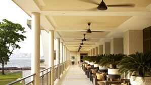 A corridor with ceiling fans, potted plants, and seating along a waterfront view.