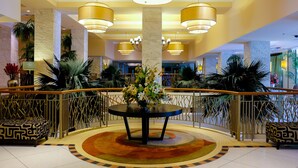 A lobby with a central round table, multiple chandeliers, and a decorative railing.