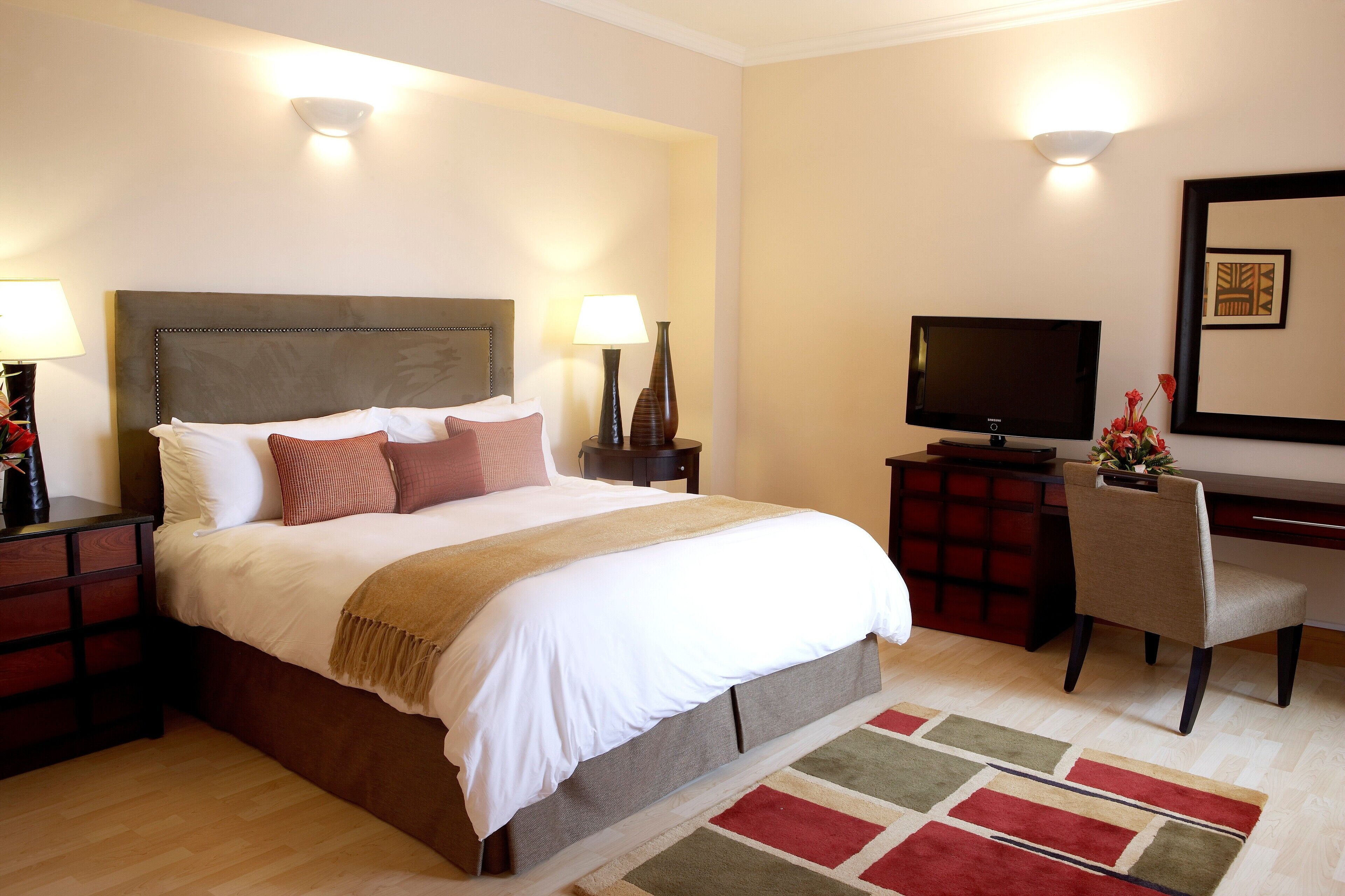 A hotel room with a large bed, bedside tables, a desk with a chair, a television, and a mirror on the wall.