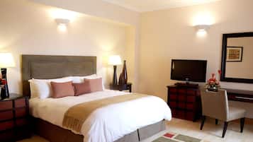 A hotel room with a large bed, bedside tables, a desk with a chair, a television, and a mirror on the wall.