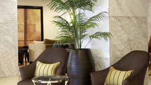A lobby with two patterned armchairs, a large potted plant, and a modern light fixture.