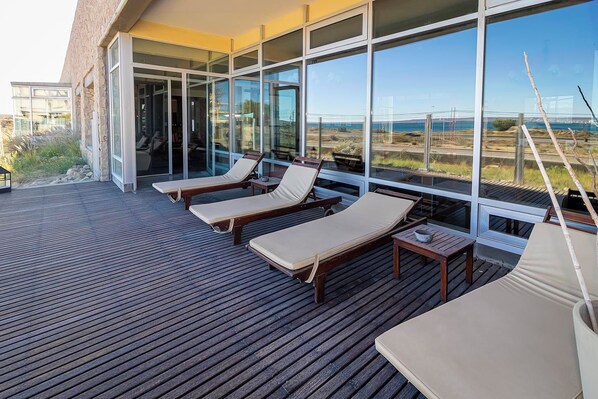 Una terraza con sillones de madera y un muro de vidrio que ofrece vistas al paisaje.