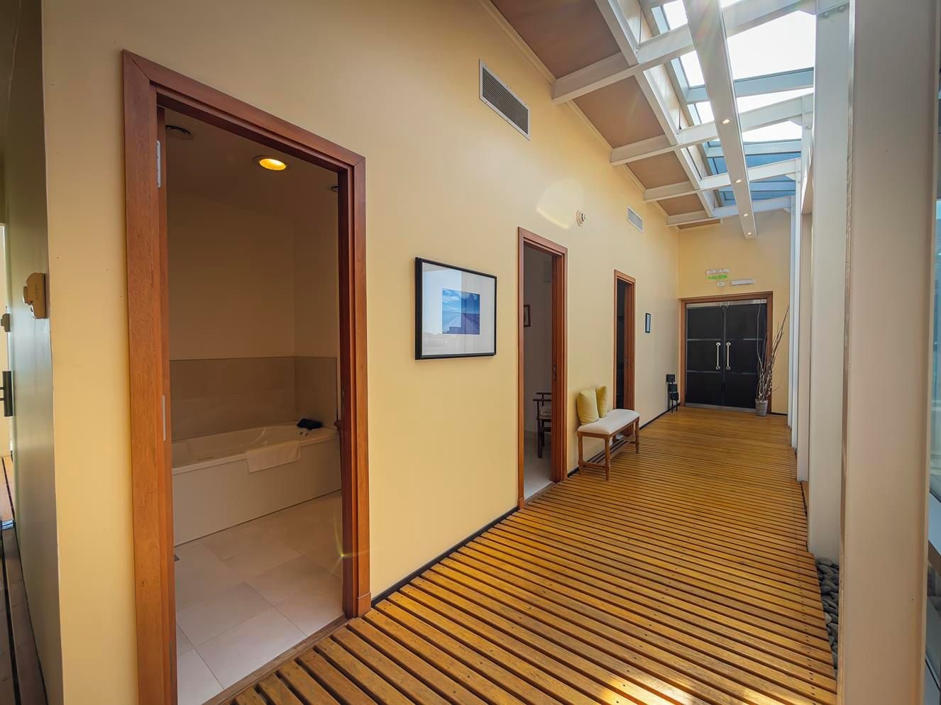 A hotel corridor with wooden flooring, a bench, and a framed picture on the wall.