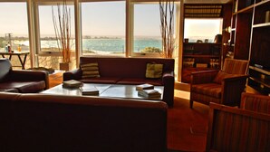 Un salón acogedor con sofá, sillones y una mesa de centro. Amplias ventanas ofrecen vistas al océano.
