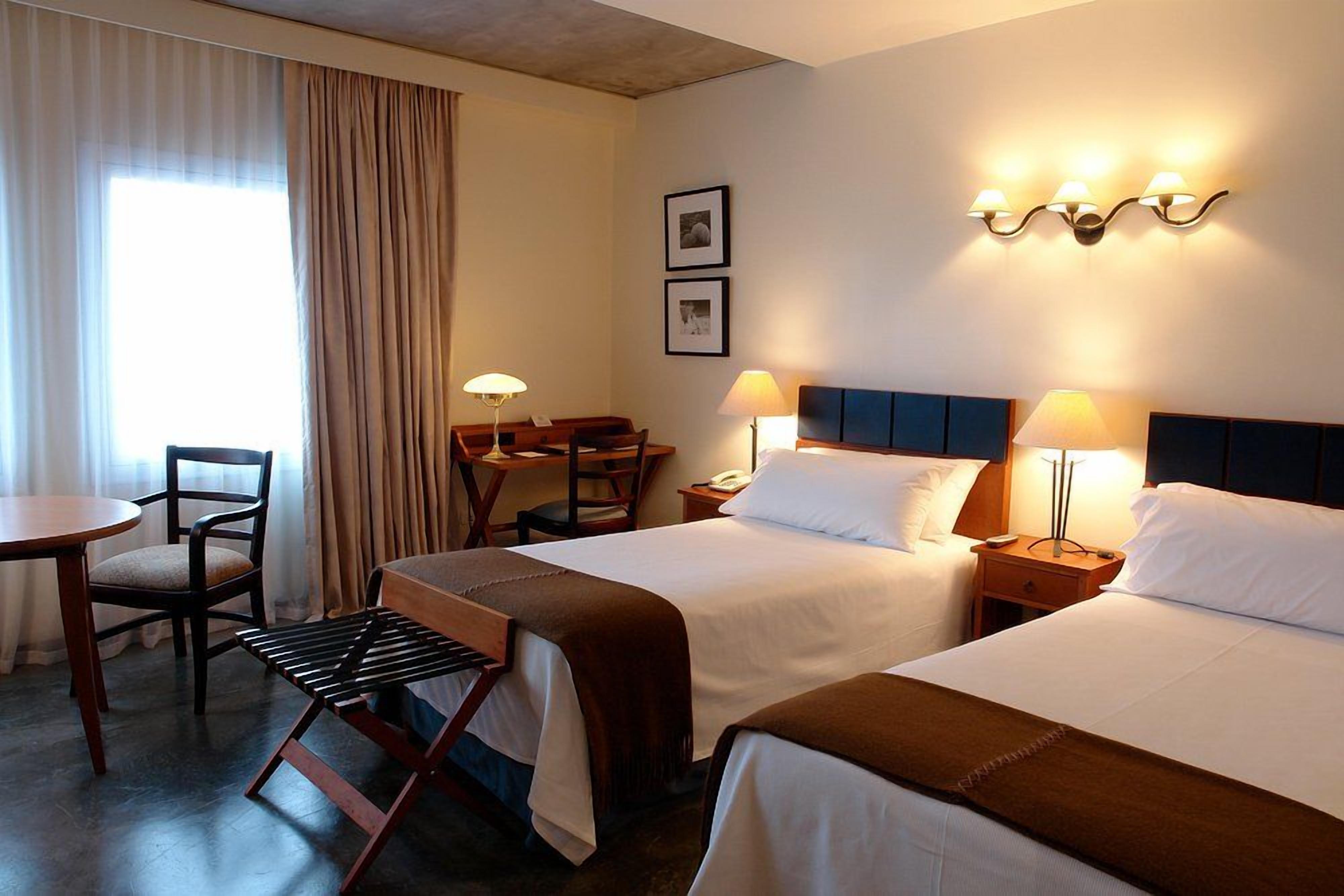 Een hotelkamer met twee bedden, een bureau, een stoel en een lamp.