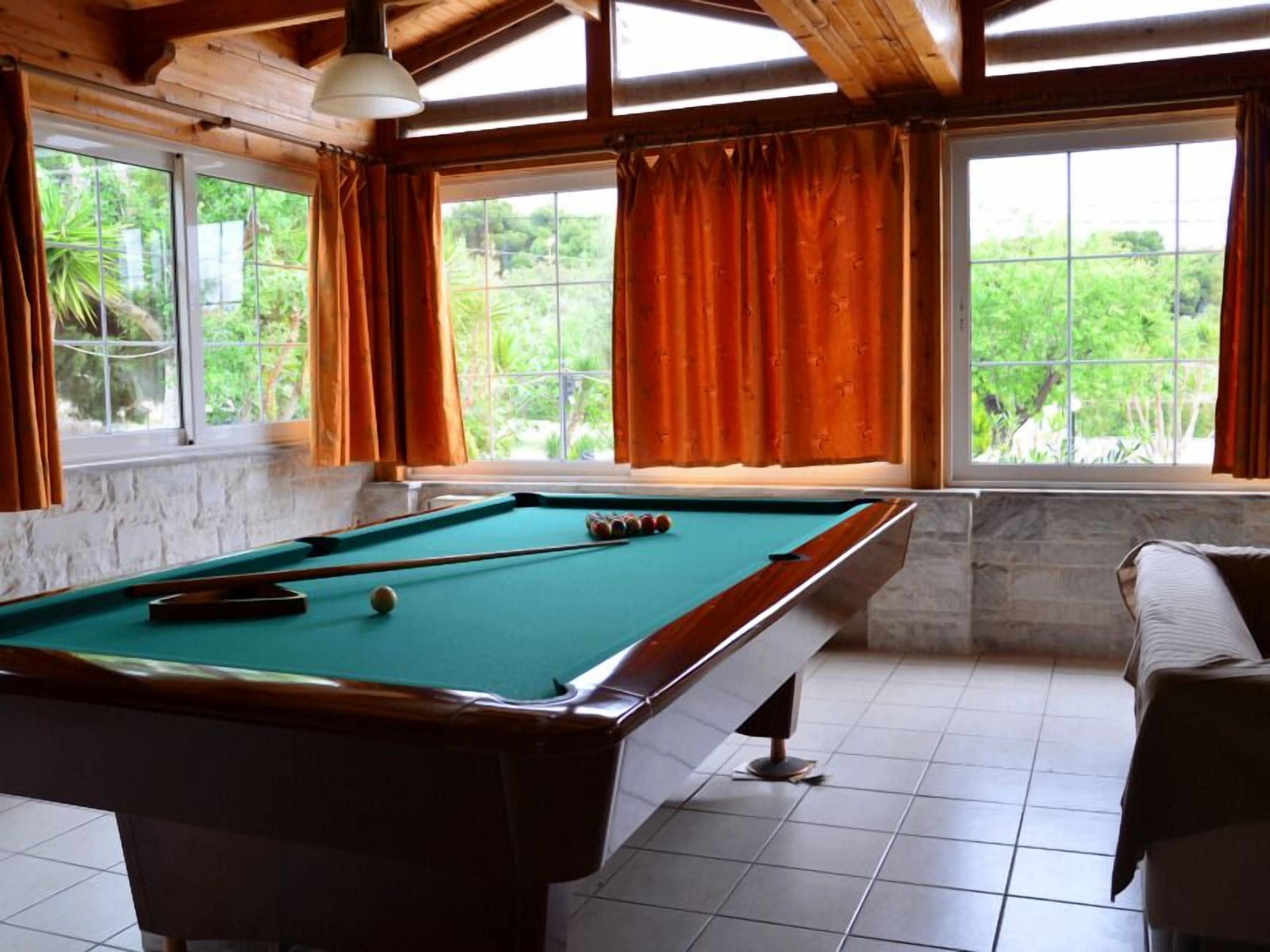 A pool table in a room with large windows and a view of greenery outside.