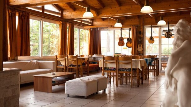 A spacious room with wooden beams, large windows, and a dining area with wooden furniture. - Saron Hotel (Lavreotiki)