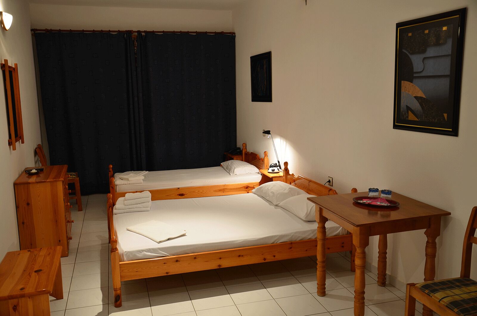 Quarto com duas camas de madeira, uma pequena mesa de madeira, uma cadeira, uma escrivaninha e um quadro na parede.