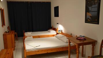 Quarto com duas camas de madeira, uma pequena mesa de madeira, uma cadeira, uma escrivaninha e um quadro na parede.