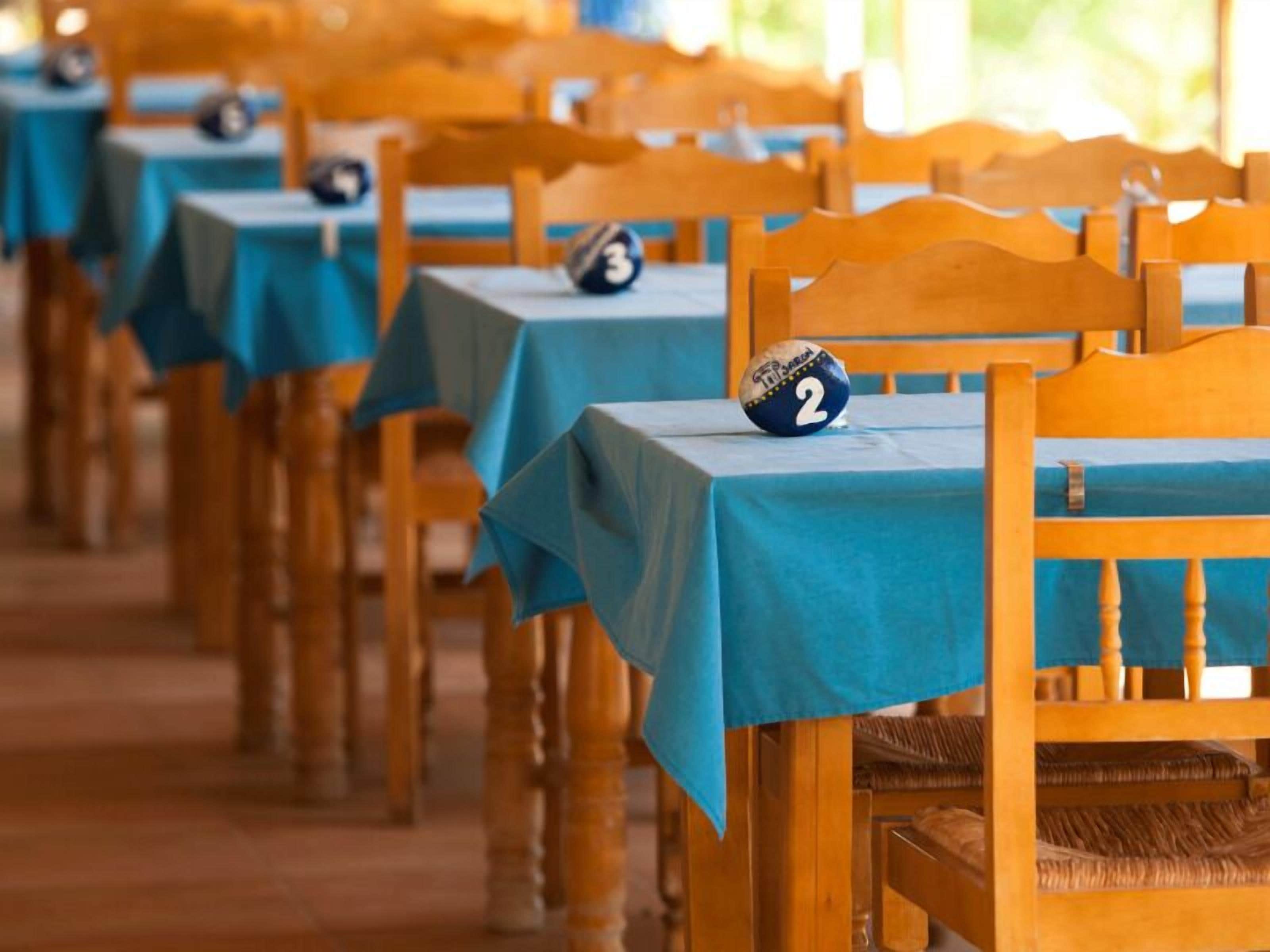 Fileiras de cadeiras de madeira com toalhas de mesa azuis e placas numeradas, indicando uma disposição de assentos para um evento ou encontro.