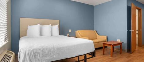 A hotel room with a bed, a chair, a small table, and a heater.