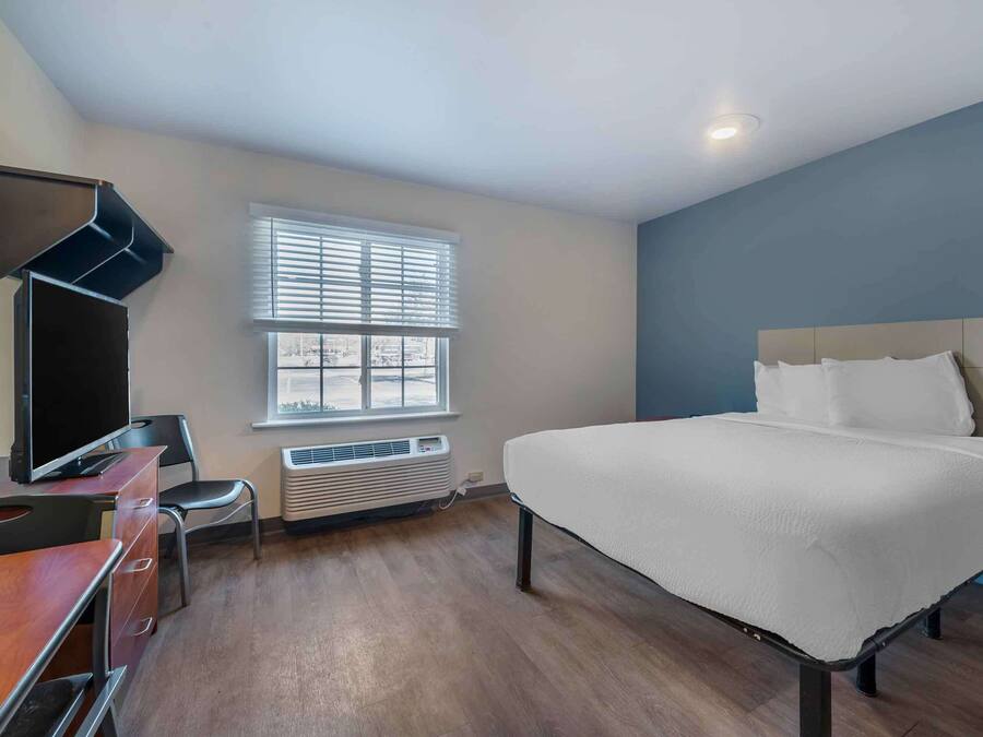 A hotel room with a bed, a desk with a chair, a TV, and a window with blinds.
