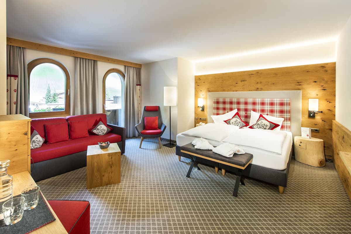 Hotellihuone, jossa on sänky, punainen sohva, tuoli, pieni pöytä ja lamppu.