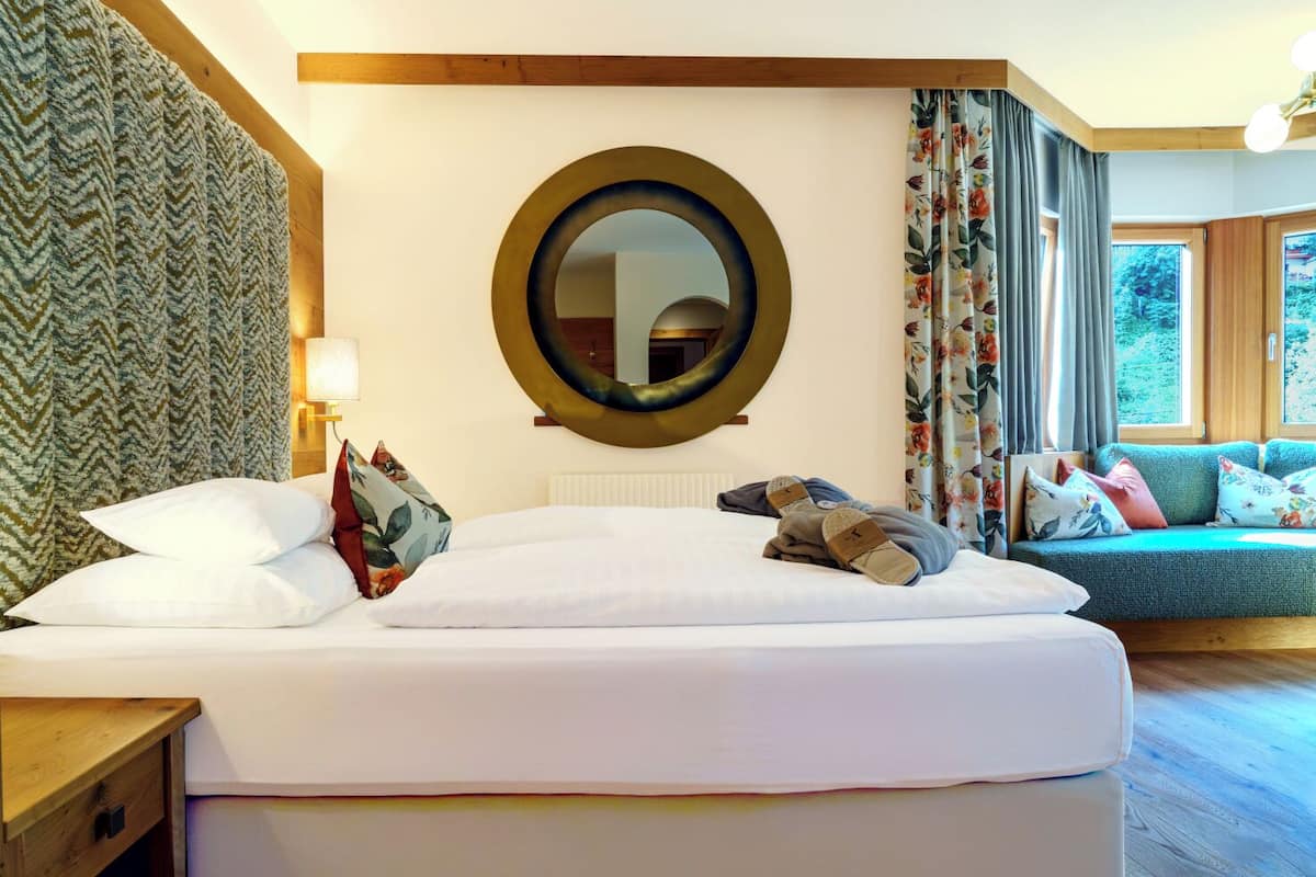 Hotellihuone, jossa on suuri sänky, pyöreä peili, sohva ja näkymä vehreään maisemaan.