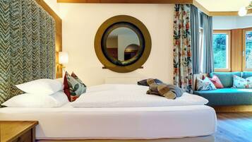 Habitación de hotel con una cama grande, un espejo redondo, un sofá y vistas a zonas verdes.